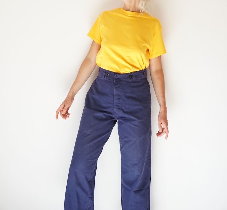 K&ouml;nnte beinhalten: Eine Person tr&auml;gt ein gelbes T-Shirt mit kurzen &Auml;rmeln und eine dunkelblaue Hose mit Knopfleiste.
