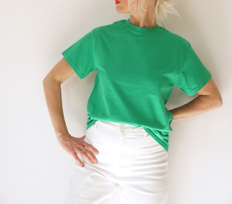 May include: A vibrant green t-shirt paired with white denim pants. The short-sleeved shirt has a crew neck and a solid color. The white pants have a button closure. The outfit is simple and casual.