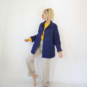 Pu&ograve; includere: Giacca blu navy con bottoni, due tasche frontali e un dettaglio con bottone rosso. Indossata sopra una camicia gialla a maniche lunghe e abbinata a pantaloni beige chiaro. L'outfit &egrave; ambientato su sfondo bianco.