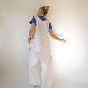 May include: A white and blue striped linen dress with a sleeveless design. The dress is worn over white trousers.