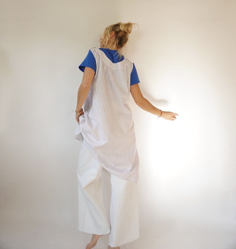 May include: A white and blue striped linen dress with a sleeveless design. The dress is worn over white trousers.