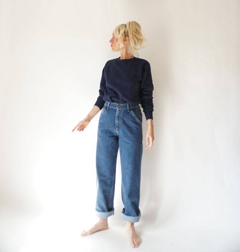 May include: A navy blue sweatshirt and blue denim jeans. The jeans have a high waist and are cuffed at the ankles. The model is wearing a casual outfit, perfect for everyday wear.