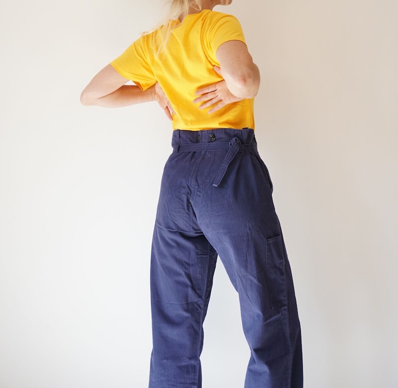 K&ouml;nnte beinhalten: Eine Person tr&auml;gt ein gelbes T-Shirt mit kurzen &Auml;rmeln und eine dunkelblaue, hochgeschlossene Hose mit G&uuml;rtel.