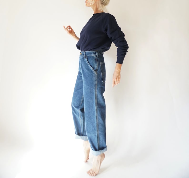 May include: A navy blue sweatshirt paired with light blue denim jeans. The jeans have a relaxed fit with a cuffed hem. The outfit is simple and casual, suitable for everyday wear. The jeans have a classic five-pocket design.