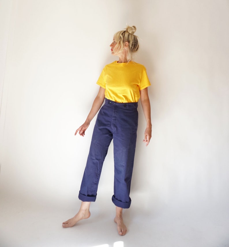 K&ouml;nnte beinhalten: Eine Frau tr&auml;gt ein gelbes T-Shirt und eine dunkelblaue, hochgeschlossene Hose mit umgeschlagenen Beinen.