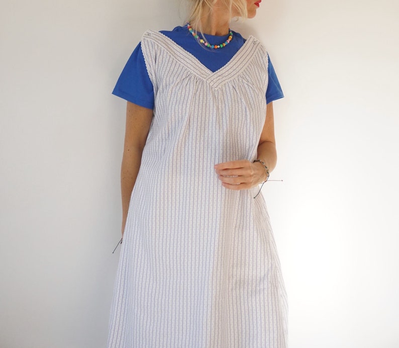 May include: A white and blue striped sleeveless dress with a V-neckline. The dress is worn over a blue t-shirt.