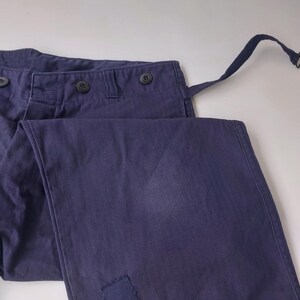 K&ouml;nnte beinhalten: Eine dunkelblaue Hose mit einem Flicken am rechten Bein. Die Hose hat einen Knopfverschluss und G&uuml;rtelschlaufen.