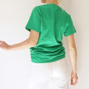 May include: A bright green t-shirt with short sleeves. The shirt is made of a soft material and is paired with white pants. The person is turned away from the camera.