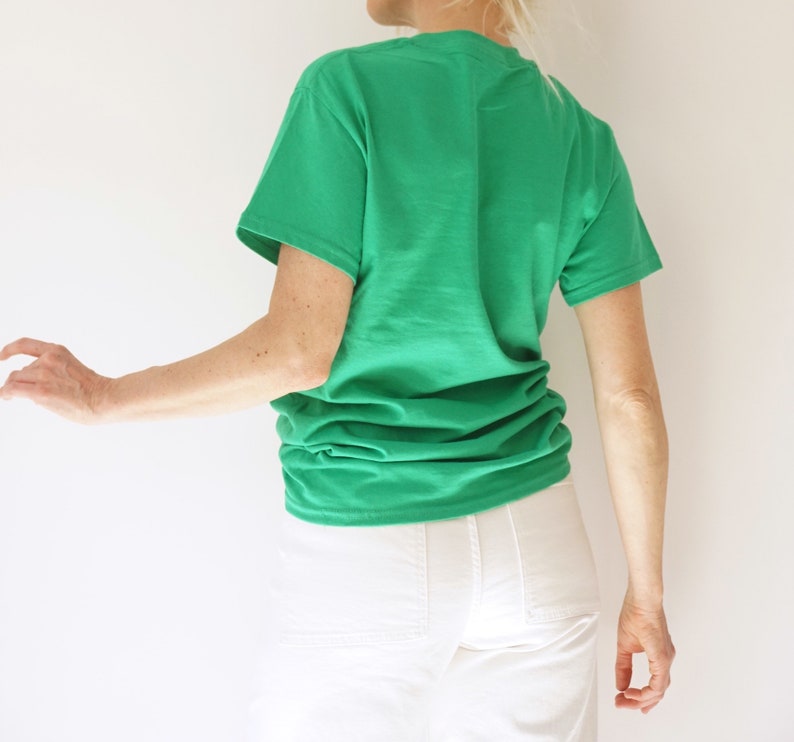 May include: A bright green t-shirt with short sleeves. The shirt is made of a soft material and is paired with white pants. The person is turned away from the camera.