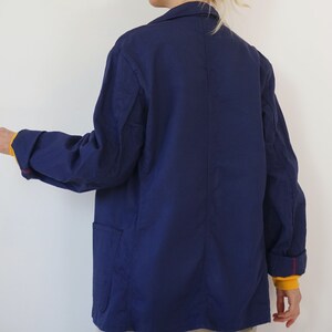 Pu&ograve; includere: Giacca blu navy con colletto e due tasche anteriori. Le maniche sono risvoltate, rivelando una fodera gialla e cuciture rosse. La giacca &egrave; realizzata in tessuto leggero.