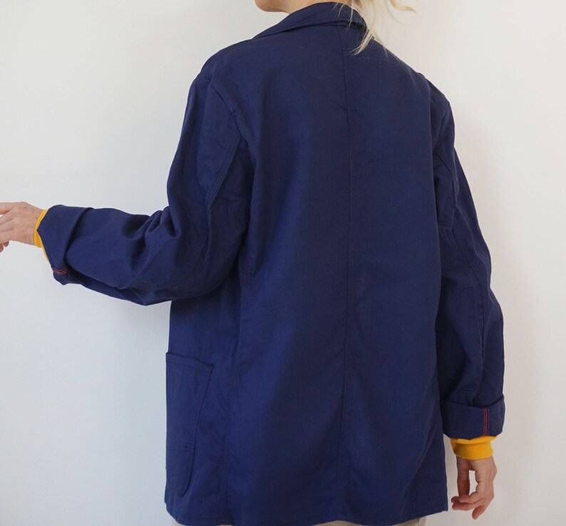 Pu&ograve; includere: Giacca blu navy con colletto e due tasche anteriori. Le maniche sono risvoltate, rivelando una fodera gialla e cuciture rosse. La giacca &egrave; realizzata in tessuto leggero.