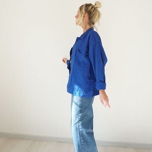 May include: A vibrant blue jacket with multiple pockets and a collared neckline. The jacket is paired with light-wash denim jeans with rolled-up cuffs. The outfit is casual and comfortable, suitable for everyday wear.