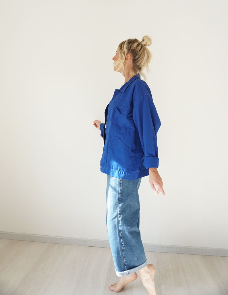 May include: A vibrant blue jacket with multiple pockets and a collared neckline. The jacket is paired with light-wash denim jeans with rolled-up cuffs. The outfit is casual and comfortable, suitable for everyday wear.