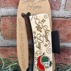 May include: Wooden hair claw with the text "Sleigh All Day" and a Christmas present design. The claw is attached to a cardboard tag with the text "Lorna Lou Home" and "Handpainted Hair Claws".