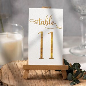 May include: Gold table number card with the word "table" and the number "11" on a small wooden easel.