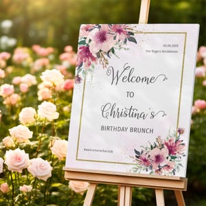May include: A white welcome sign with a gold frame and pink floral accents. The sign reads "Welcome to Christina's Birthday Brunch #welcometotheclub".