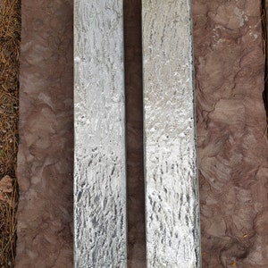 May include: Two rectangular pieces of glass with a textured, silver-like finish. The glass is sitting on a brown, textured surface.