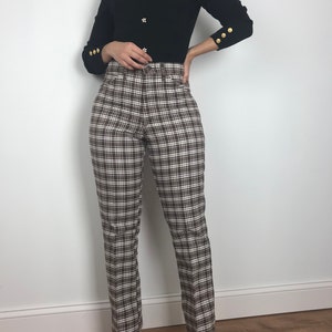 May include: A black mock neck sweater with gold buttons on the front and cuffs. The sweater is paired with brown and white plaid pants.