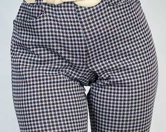 May include: Cream-colored belt with a large, rounded buckle and a crocodile-skin texture. The belt is worn with houndstooth-patterned pants in black, white, and brown. The pants are high-waisted.