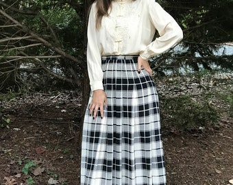 May include: A woman wearing a white blouse with lace detailing and a black and white plaid skirt. She is wearing black lace-up boots.