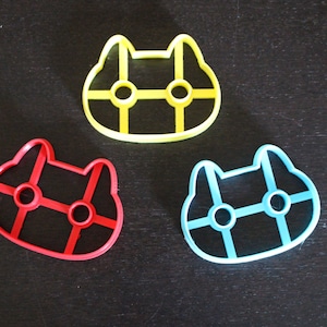 May include: Three plastic cookie cutters shaped like cats. The cutters are yellow, red, and blue.