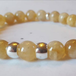 May include: A bracelet made of golden-yellow gemstone beads and silver-coloured metal beads. The beads are strung together, creating a flexible bracelet. The gemstones have a polished finish, reflecting light. The bracelet is a piece of jewellery.
