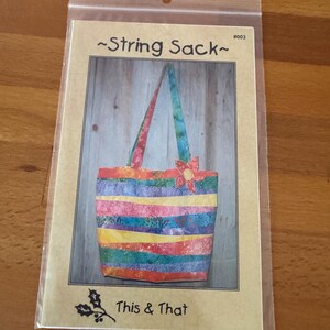 May include: A package featuring a colorful String Sack pattern. The image shows a completed tote bag with a patchwork design in various colors, including red, yellow, blue, and green. The bag has matching handles and a flower embellishment. The text "This & That" is visible.