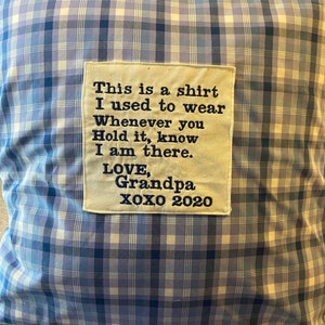 May include: A blue and white plaid pillow with a white fabric patch sewn on the front. The patch has black embroidered text that reads: "This is a shirt I used to wear Whenever you Hold it, know I am there. LOVE, Grandpa XOXO 2020"