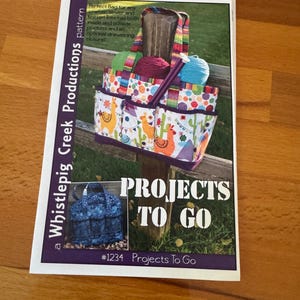 May include: A colorful tote bag with a llama and cactus pattern, filled with yarn and knitting supplies. The bag has multiple pockets and a rainbow strap. The text "PROJECTS TO GO" is displayed on the image.