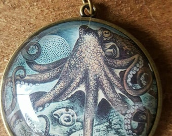 Op de afbeelding: Een ronde hangerketting met een gedetailleerde illustratie van een octopus in blauw, bruin en wit. De hanger heeft een bronzen frame en hangt aan een delicate goudkleurige ketting. Het octopusontwerp is geïnspireerd op vintage.