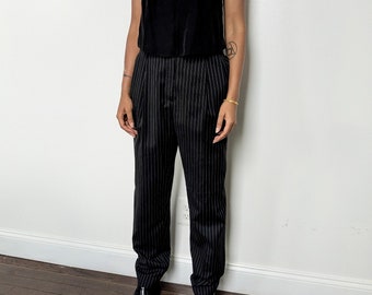 May include: A black sleeveless top with a V-neckline and black and white striped pants. The person is wearing black shoes.