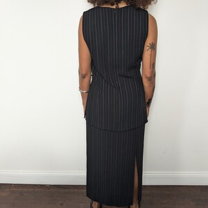 May include: A black and white striped sleeveless dress with a slit in the skirt. The dress has a fitted bodice and a flowing skirt.