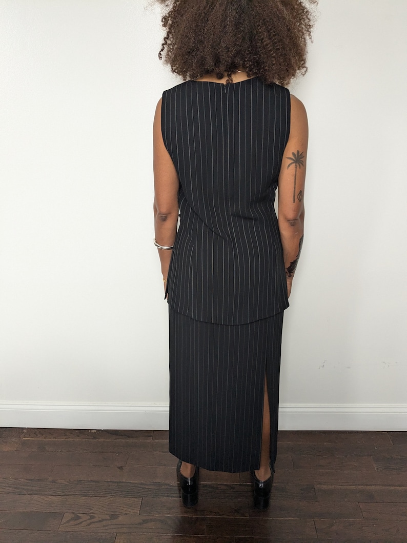 May include: A black and white striped sleeveless dress with a slit in the skirt. The dress has a fitted bodice and a flowing skirt.