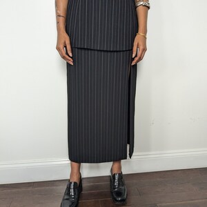 May include: A black and white pinstripe skirt with a side slit. The skirt is knee-length and has a fitted silhouette.