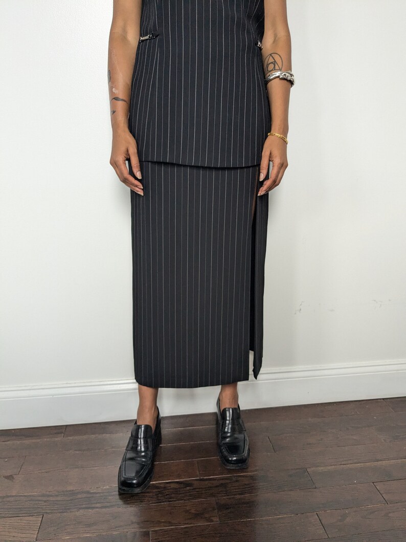 May include: A black and white pinstripe skirt with a side slit. The skirt is knee-length and has a fitted silhouette.