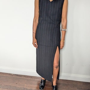 May include: A black and white striped sleeveless maxi dress with a side slit. The dress has a v-neckline and a relaxed fit.