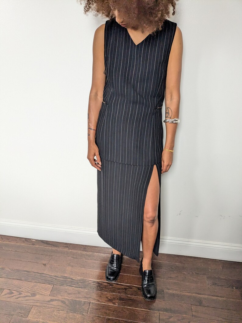 May include: A black and white striped sleeveless maxi dress with a side slit. The dress has a v-neckline and a relaxed fit.