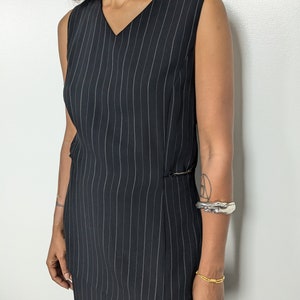 May include: A black and white striped sleeveless dress with a v-neckline and a side slit. The dress is made of a lightweight fabric and has a relaxed fit.