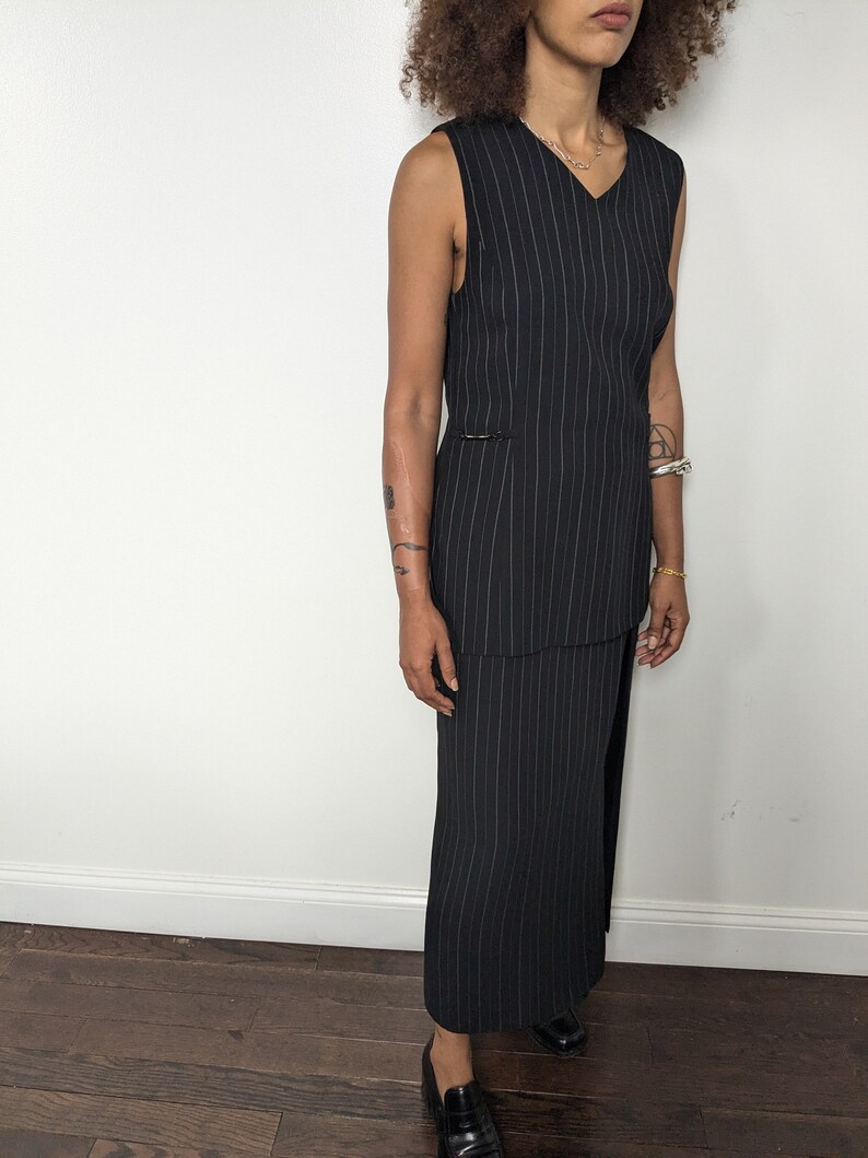 May include: A black and white striped sleeveless dress with a V-neckline. The dress has a fitted bodice and a flowing skirt.
