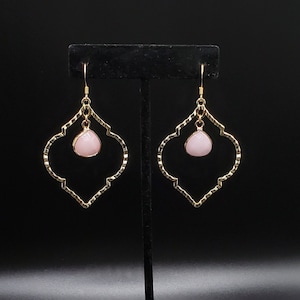 May include: A pair of gold earrings with a pink teardrop-shaped stone hanging from each earring. The earrings are in the shape of a quatrefoil.