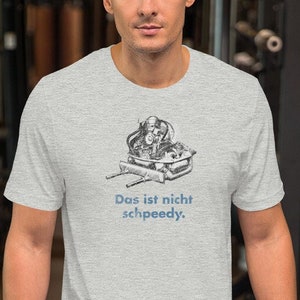 Pode incluir: Uma camiseta cinza com uma ilustração em preto e branco de uma pessoa em um veículo pequeno. O texto na camiseta diz "Das ist nicht schpeedy."
