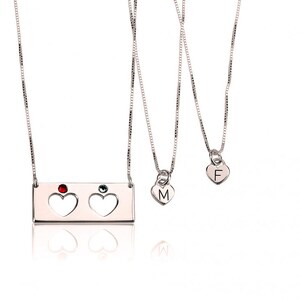 May include: Three silver necklaces with heart pendants. The top necklace has a rectangular charm with two cut-out hearts and red and green gemstones. The middle necklace has a heart pendant with the letter "M" and the bottom necklace has a heart pendant with the letter "F".
