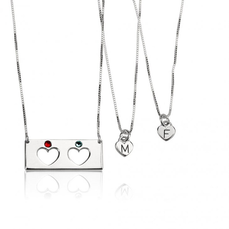 May include: Three silver necklaces with heart pendants. The top necklace has a rectangular pendant with two cut-out hearts and red and blue gemstones. The middle necklace has a heart pendant with the letter "M" and the bottom necklace has a heart pendant with the letter "F".