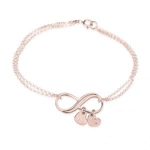 May include: A rose gold infinity bracelet with two small heart charms. The charms are engraved with the initials "M" and "R".
