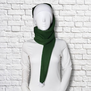 May include: A long, dark green fleece scarf with a white pom-pom at the end, draped around the neck of a white mannequin wearing a white long-sleeved shirt and a white beanie. The scarf is made of a soft, solid-coloured fabric with a smooth texture.