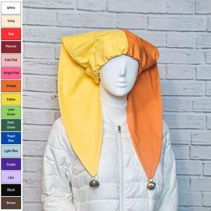 May include: A two-toned jester hat featuring a bright yellow left side and an orange right side. The hat is constructed from fabric with a gathered crown and two long, pointed ear-like flaps that hang down, each finished with a small metal bell.