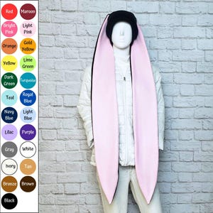 Könnte beinhalten: Eine schwarze Mütze mit langen, übergroßen, hellrosa Hasenohren, die bis zur Taille herabhängen. Die Mütze wird auf einer Schaufensterpuppe mit einer weißen Steppjacke präsentiert. Eine Farbkarte auf der linken Seite listet Optionen wie Rot, Kastanienbraun, Pink, Orange, Gelb, Grün, Blau, Lila, Grau, Weiß, Elfenbein, Hellbraun, Bronze, Braun und Schwarz auf.