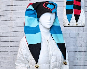 May include: A whimsical jester hat with a black top featuring a heart design, and long, striped blue and black panels. The hat has a red trim and gold bells at the tips. The hat is displayed on a mannequin wearing a white jacket.