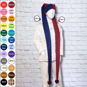 May include: A long, two-toned jester-style hat featuring a deep navy blue side and a maroon side, with matching pom-poms at the ends. The hat is displayed on a mannequin wearing a white quilted jacket and white pants, alongside a color chart.