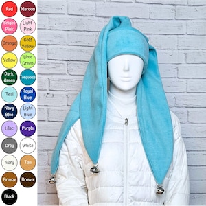 May include: A turquoise fleece hat with two long, pointed ear-like flaps hanging down on either side. Each flap terminates in a small, metallic silver bell. The hat is displayed on a mannequin wearing a white quilted jacket, with a color chart.